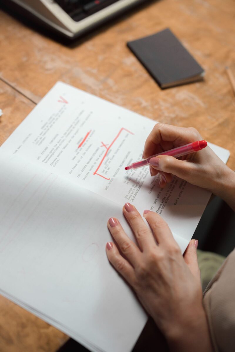 A hand proofreading printed pages with a red pen, checking them carefully