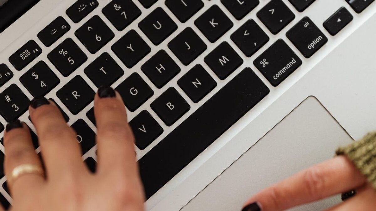 Hands typing on a laptop keyboard, writing an article